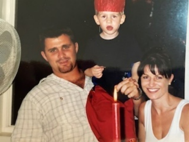 Family photo of a man, woman, and young child smiling together, with the child wearing a red paper crown
